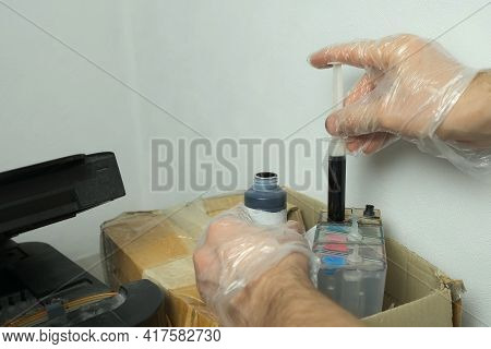 Man Puts Black Ink In A Printer Using A Syringe, Hands In Gloves Closeup. Dials Ink Into A Syringe F