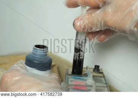 Man Puts Black Ink In A Printer Using A Syringe, Hands In Gloves Closeup. Dials Ink Into A Syringe F