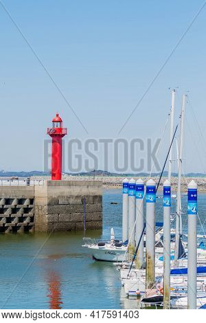 Red Lighthouse On Pier Overlooking Yachts.