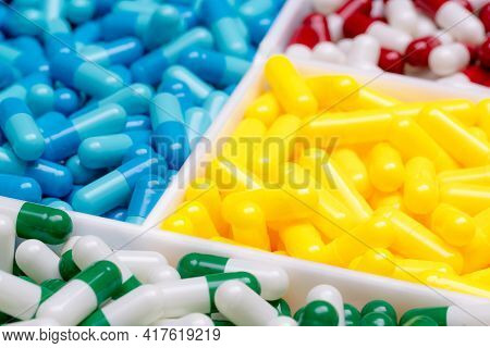 Selective Focus On Green-white Capsule Pills On Blurred Yellow, Blue, Red-white Capsules Pill. Drug 