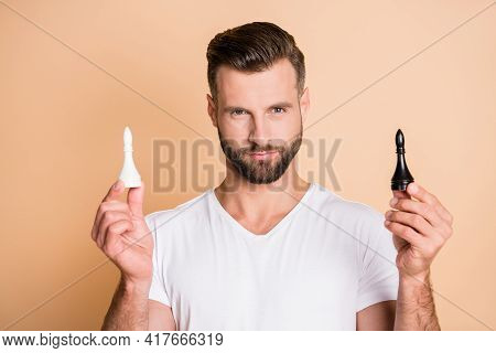 Portrait Of Attractive Content Virile Guy Holding In Hands Two Chess Pieces Isolated Over Beige Past
