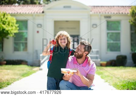 Parent And Pupil Of Primary School Go Hand In Hand. Schoolboy And Parent In Shirt Holding Lunch Box.
