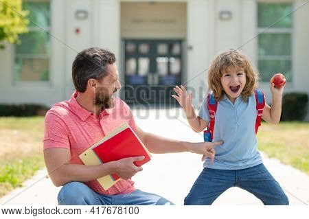 Parent And Amazed Pupil Of Primary School Go Hand In Hand. Teacher In T-shirt And Excited Schoolboy 