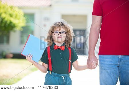 Portrait Of Happy Nerd Pupil Holding Teachers Hand. Father Holding Hand Of Son With Backpack Outdoor