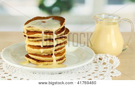 หวาน pancakes บนแผ่นกับนมข้นบนโต๊ะในห้องครัว