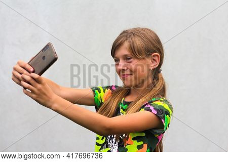 A Ten Year Old Girl Poses And Takes A Selfie With Her Hand On Her Phone In A Brown Case. Gray White 