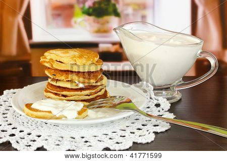 หวาน pancakes บนแผ่น ด้วยครีมเปรี้ยวบนโต๊ะในห้อง