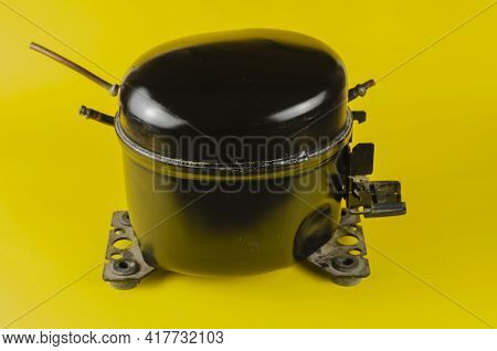 Black Refrigerator Motor-compressor On Yellow Background. Old Hermetic Piston Compressor. Device Des
