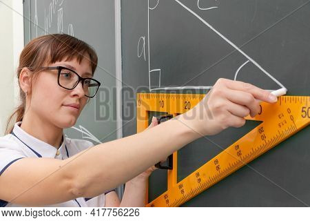 School Teacher Young Woman In The Class At The Blackboard Draws A Triangle With A Ruler. Portrait. C