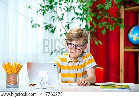Smart Child With Glasses Using Tablet Laptop Computer At Home Interior. Child Writing Homework. Teen