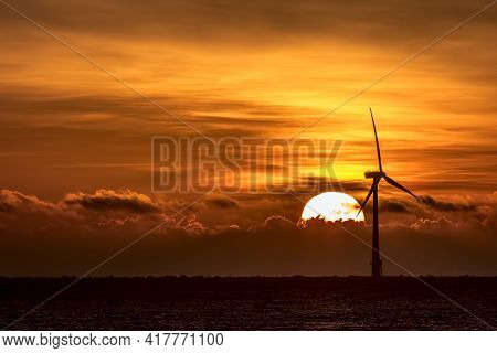 Tropical Sunset Background Image With Wind Turbine On Sea The Horizon. Deep Orange Sky With Sun Sett