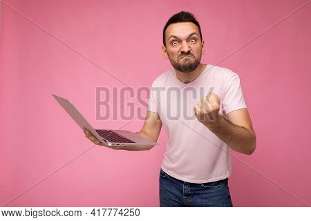 Handsome Angry And Wrathful Man Holding Laptop Computer Showing Fist Looking At Camera In T-shirt On