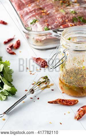 Close Up View Of A Jar Of Homemade Lime And Cilantro Marinade With A Raw Flank Of Beef In Behind.