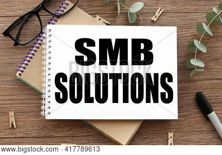 Smb Solutions.on A Wooden Background There Are Two Notepads Near Glasses And A Black Felt-tip Pen.