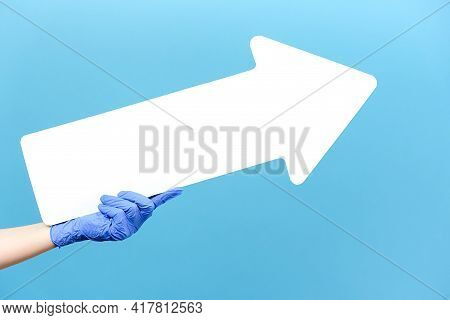 Close Up Of Male In Medical Protective Blue Gloves Hold White Arrow Pointing At Copy Space For Adver