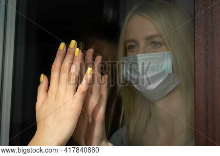 Isolation Of The Coronavirus. An Unhappy Young Blonde Woman In A Mask Touches A Woman's Hand Through