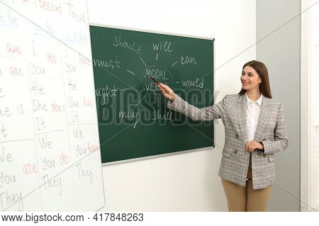 English Teacher Giving Lesson On Modal Verbs Near Chalkboard In Classroom