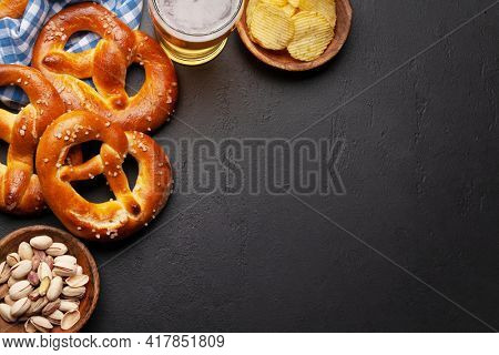 Lager beer mug, nuts, potato chips and fresh baked homemade pretzel with sea salt on stone table. Classic beer snack. Top view flat lay with copy space