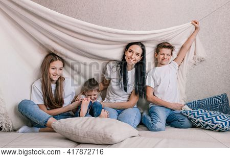 Happy Family Mom And Small Children Laugh Merrily Sitting On The Sofa Covered With A White Blanket. 