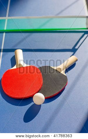 duas pás do tênis de mesa ping pong e a bola branca na placa azul