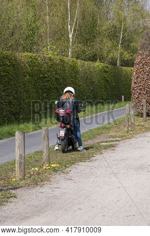 Sint Gillis Waas, Belgium, April 21, 2021, Girl On Scooter Stops And Looks At Her Smartphone