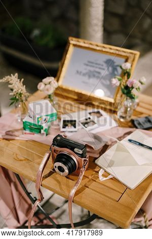 On A Wooden Table Is An Orange Fujifilm Instax Square Sq1 Camera With Spare Film Cartridges And Inst