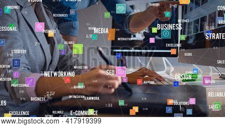 Composition of digital icons and business text over woman using computer and graphic tablet. global technology and digital interface concept digitally generated image.