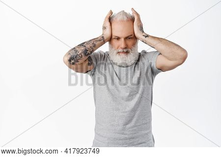 Annoyed And Distressed Old Man With Tattoos, Holding Hands On Head With Troubled Upset Face, Looking