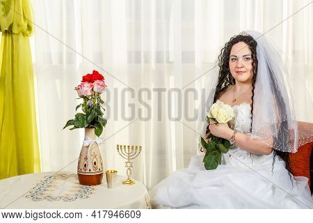 A Happy Jewish Bride With A Bouquet Of White Roses Sits In The Synagogue Before The Huppa Ceremony A