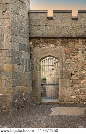 Ancient Stone Wall With A Gate In The Old Castle. Wooden Gate Of A Medieval Castle