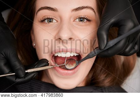 Close Up Of Dentist Hands In Black Sterile Gloves Examining Female Patient Teeth With Dental Mirror 