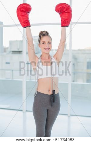 Victorious sporty blonde wearing red boxing gloves cheering in bright room