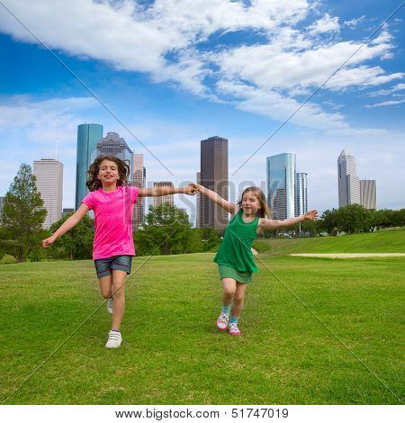 Two sister girls friends running holding hand in urban modern skyline on grass lawn