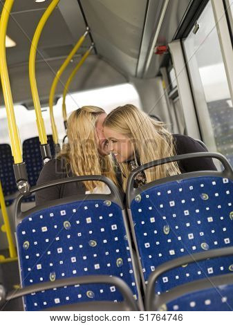 Two young women whispering secrets on the bus