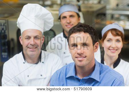 Young manager posing in a kitchen with chefs smiling at camera