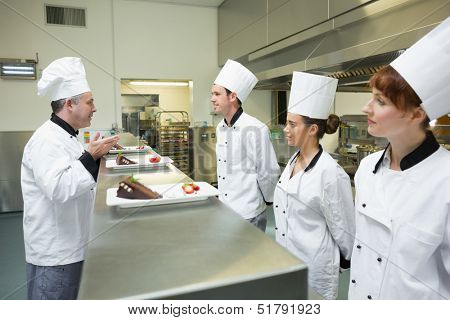 Tre cuochi che presentano i loro piatti da dessert per lo chef in cucina occupato