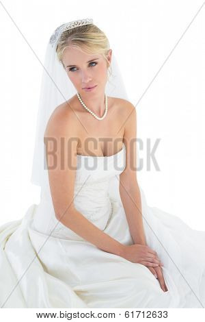Thoughtful young bride in off shoulder dress sitting against white background