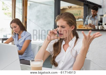Annoyed young woman using mobile phone in the coffee shop