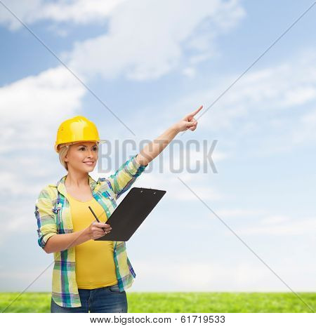 repair, construction and maintenance concept - smiling woman in helmet with clipboard pointing finger