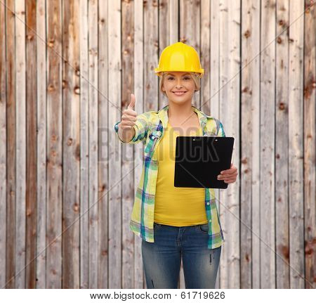 repair, construction and maintenance concept - smiling woman in helmet with clipboard showing thumbs up