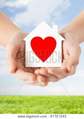 charity, real estate and family home concept - closeup picture of female hands holding white paper house with red heart