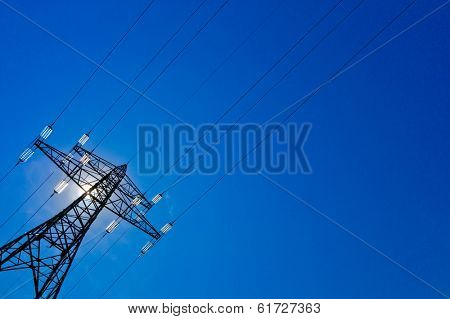 the current mast of a high voltage line with sun and blue sky. energy supply by power line.