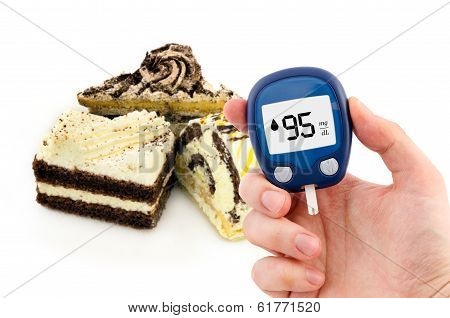Hand Holding Meter. Diabetes Doing Glucose Level Test. Cake In Background