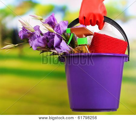 Housewife holding bucket with cleaning equipment on bright background. Conceptual photo of spring cleaning. 
