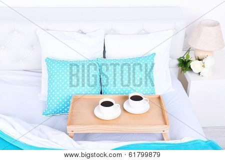 Cups of coffee on comfortable soft bed with pillows