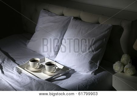 Cups of coffee on comfortable soft bed with pillows