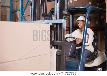 Forklift driver operating machine with boxes on it in a large warehouse