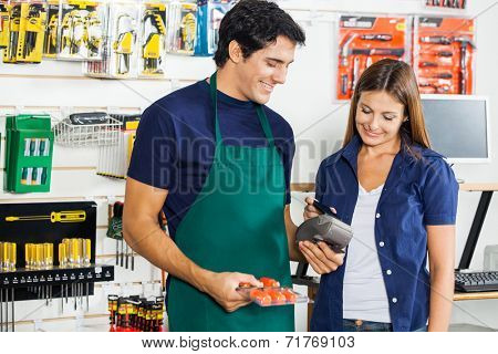 Worker accepting payment through smartphone from woman in hardware store