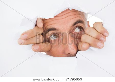 Close up of mature man peeking through torn white surface