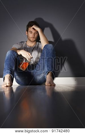 Young man with bottle of whiskey sitting on floor, drinking.